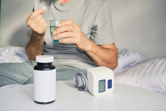 Man taking pill with water, with blood pressure monitor and medicine bottle nearby