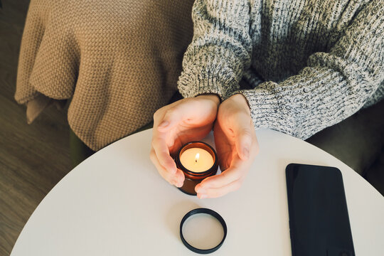 Person's hands cupping lit candle on white table, creating warm and cozy mood