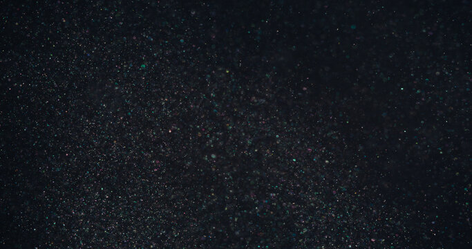 Defocused glitter. Shimmer art. Gleam pink blue green color round radiant texture floating on abstract bokeh light dark black background.