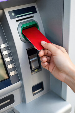 Close up of woman hand inserting red credit card into atm machine. Person uses automated teller machine for cash withdrawal bank transaction. Financial service concept with plastic card, banking