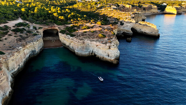 Amazing scenic drone aerial view of the beach and ocean with calm waves during a sunset with vibrant colors. Algarve, Portugal. Clear waters. Holidays and Vacations. Background. Beach with rocks. 