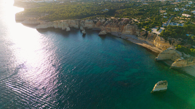 Picturesque coastal landscape of rugged limestone cliffs and clear turquoise water. Rocky cape over sea bay with stony shore under sunlight. Algarve, Portugal