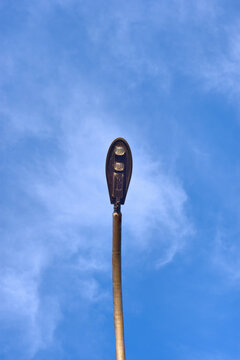 Low angle minimalist view of a modern energy-efficient LED street light pole standing tall against a clear blue sky with soft wispy clouds in Cox's Bazar, Bangladesh.
