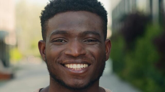Close up pensive African American man look away thinking turning looking at camera smiling toothy with healthy teeth cheerful positive happy ethnic guy smile optimistic male face outdoors in city
