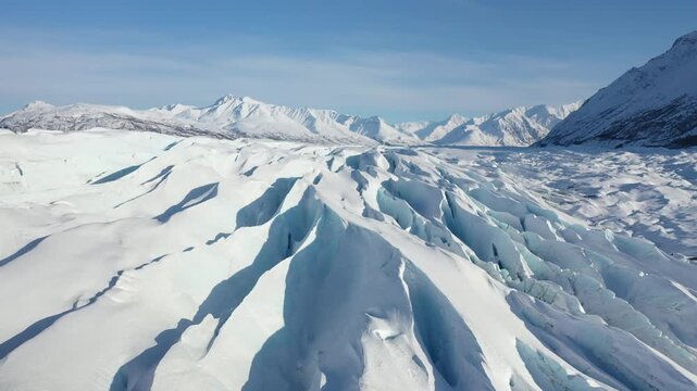 Low Aerial Flyover Above Frozen Glacial Field Toward Alpine Peaks