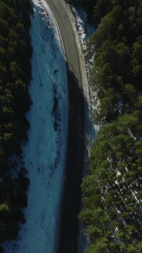 Drone footage of a curving asphalt road cutting through dense conifer forest with snow along the shoulders, winter landscape in the Ural Mountains, Russia