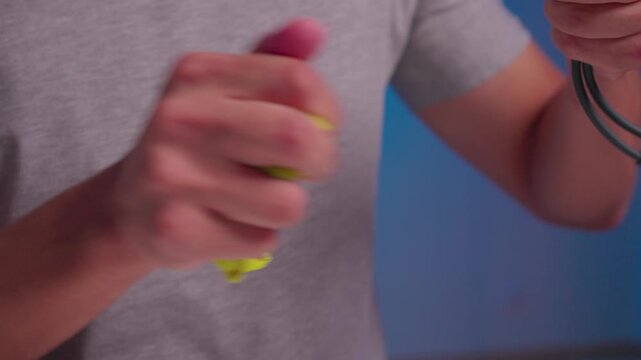 Hands twisting and wringing neon green microfiber cloth around small black connector and cable while wiping contacts with focused grip, textured folds, and pressure in studio close-up