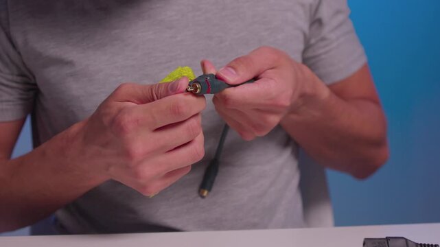 Hands twisting and wringing neon green microfiber cloth around small black connector and cable while wiping contacts with focused grip, textured folds, and pressure in studio close-up