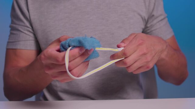 Hands twisting and wringing neon green microfiber cloth around small black connector and cable while wiping contacts with focused grip, textured folds, and pressure in studio close-up