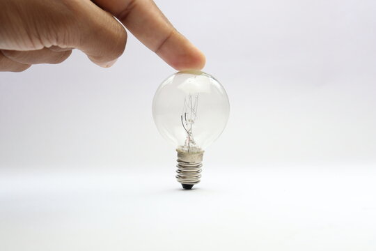 Finger touching the top of an incandescent bulb with visible screw base