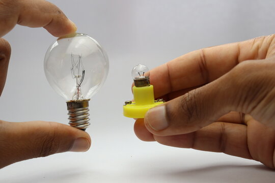 Hand holding two different types of incandescent light bulbs for comparison