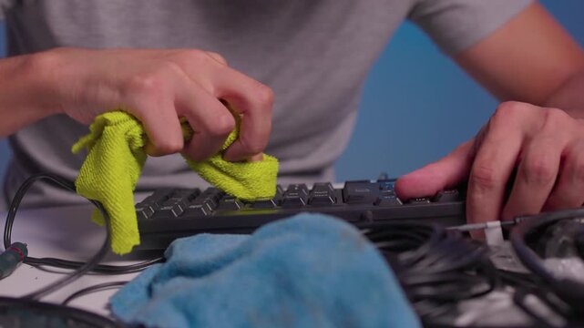 Hands cleaning computer keyboard with brush and microfiber cloth in close-up maintenance shot