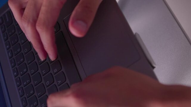 Hands typing on laptop keyboard in close view with fingers pressing keys, subtle movement and focused work at desk under cool indoor light during office routine