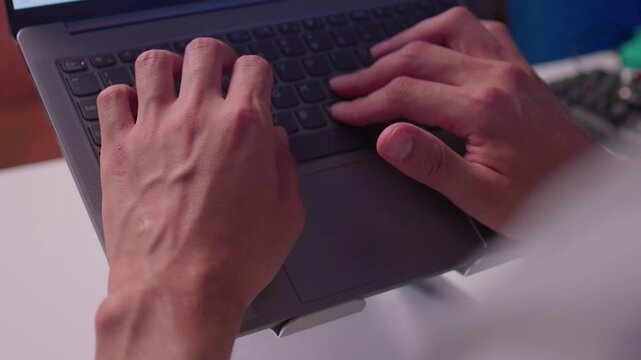 Close-up right hand adjusting tilted laptop mounted on adjustable metal hinge bracket with visible cables, reflecting soft light on aluminum housing in indoor workspace