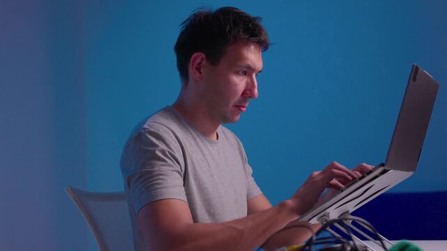 Close-up right hand adjusting tilted laptop mounted on adjustable metal hinge bracket with visible cables, reflecting soft light on aluminum housing in indoor workspace