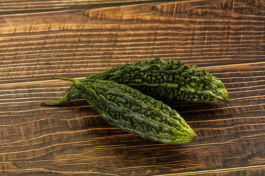 Two green bitter gourds with bumpy skin resting on dark wooden surface showing natural texture and ridges