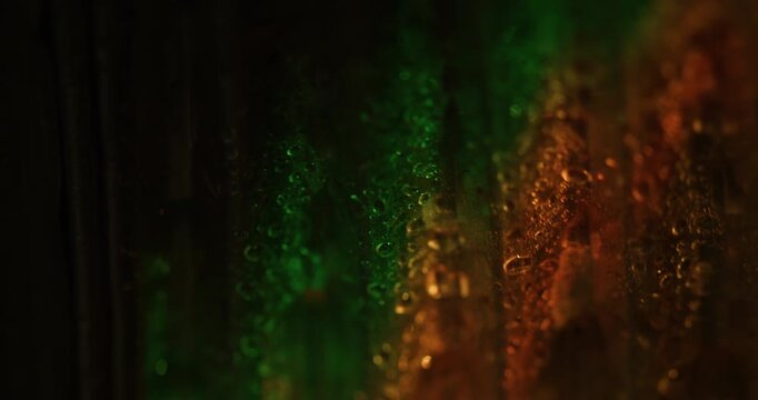 Water background. Wet texture. Defocused green orange colorful radiant bubbles glare foil reflection on art illuminated dark black abstraction.