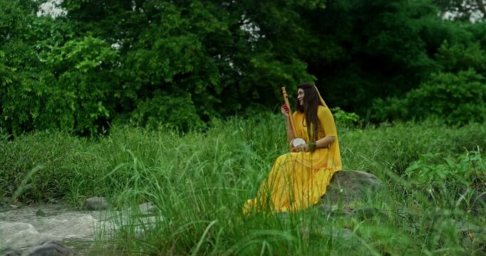 Saint Mirabai expressing deep devotion to Lord Krishna while seated in nature during gentle monsoon rain, holding a traditional ektari and prayer beads