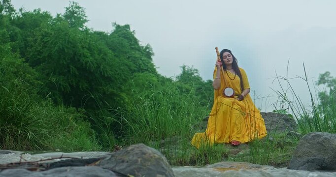 Saint Mirabai expressing deep devotion to Lord Krishna while seated in nature during gentle monsoon rain, holding a traditional ektari and prayer beads
