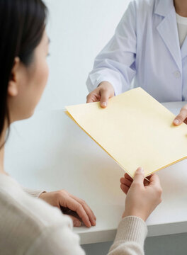 Female doctor hands yellow folder with medical results to patient in clinic. Pro physician gives health report, documents to client during consultation. Woman receives important medical info test