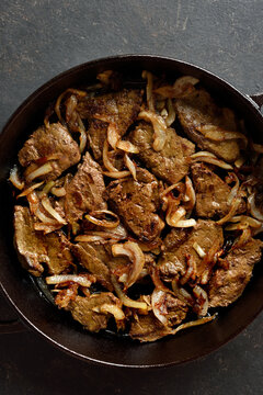Sauteed liver with butter and onion in pan on black stone background