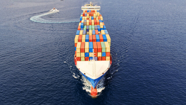 Aerial drone drone point of view photo above huge fully loaded container ship with colorful containers overlooking deep blue sea near logistics port