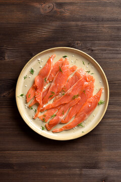 Slices of salted salmon on plate on dark wooden background