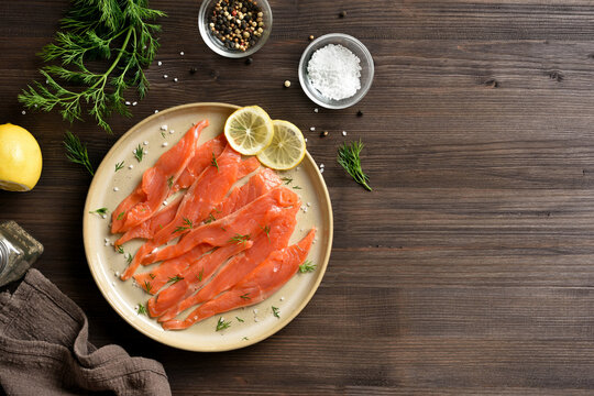 Slices of salted salmon on plate on dark wooden background