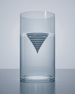 A tall clear glass vessel containing a blue conical vortex shape submerged in water against a neutral light gray studio background setting