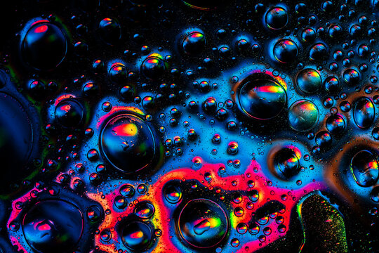 Oil and water droplets creating colorful abstract patterns with light reflections and vibrant neon hues