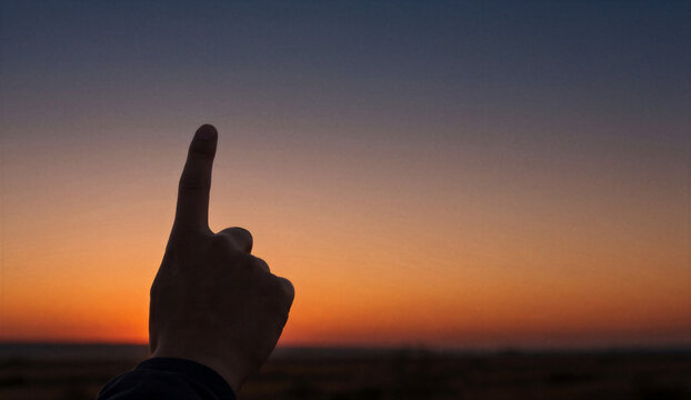 Sunset silhouette hand pointing upward with an extended single finger against an open plain nature sky