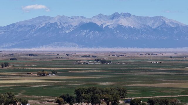 Aerial of Sangre de Cristo Mountains overlooking agricultural fields and farm buildings near La Jara Colorado in summer