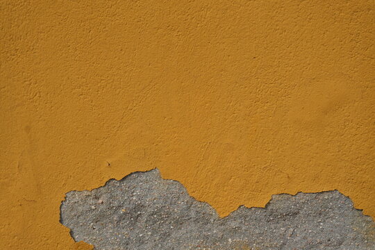 Peeling ochre plaster wall exposing rough aggregate with copy space