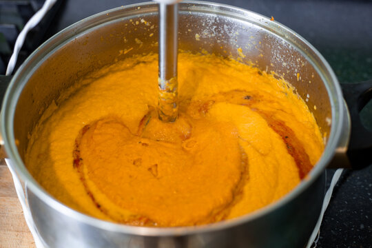 A close up of an electric immersion blender pureeing homemade squash caviar inside a stainless steel pot. Traditional Eastern European zucchini spread cooking process. Food theme.