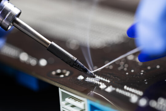 Close-up hand technician repairing broken computer with electric soldering Iron