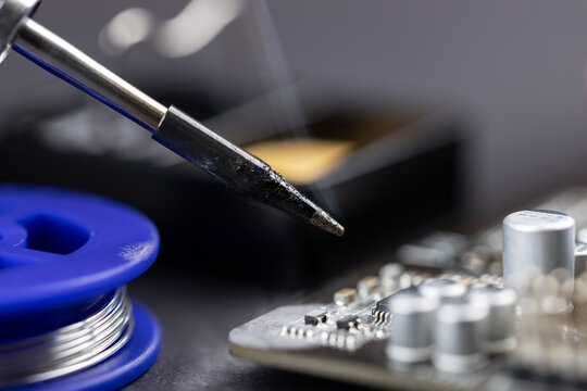 technician soldering on a brown PCB with visible flux smoke during electronics assembly at a factory workstation