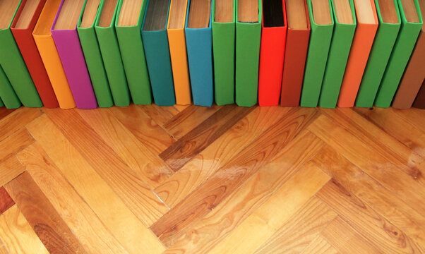 Books with multicolored covers are lined up on the parquet floor.