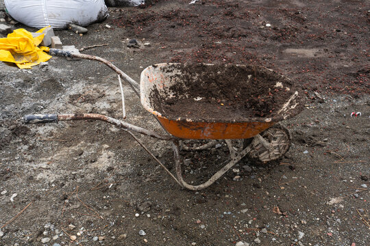 Old metal wheelbarrow at a construction site in Batumi, Georgia, surrounded by soil, stones and building materials.