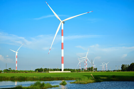Wind turbines with red and white striped poles generating clean energy in a green field under a clear blue sky.