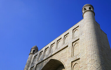 A low-angle view highlights the detailed brickwork, arched niches, and corner minarets of a traditional Islamic monumental portal under a clear blue sky in Tashkent, Uzbekistan © Gregory
