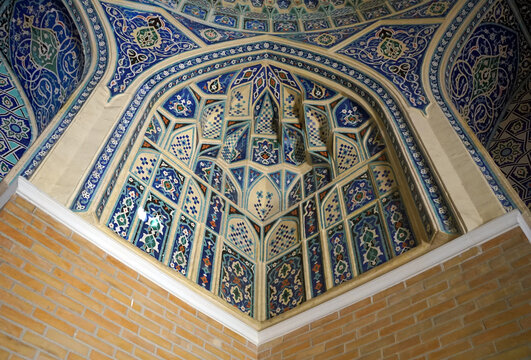 An ornate corner squinch adorned with intricate blue, white, and gold painted geometric motifs and muqarnas corbeling transitions between the brick walls and ceiling of a historic building in Tashkent