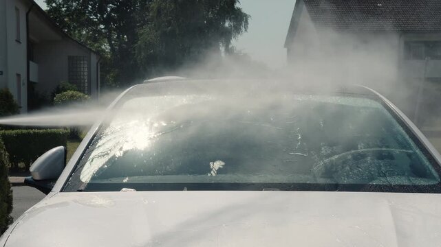 Car washer doing manual foam washing in auto detailing service. Hand washing with foam and spraying in garage. Professional car valeting. Car wash. Car in washing process. Carwash station