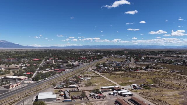 Aerial of residential and commercial buildings and US highway 285 in town of Alamosa Colorado under a blue sky with mountains in the distance