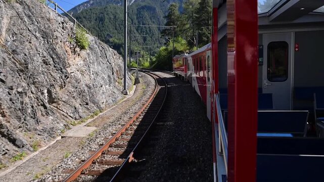 Davos, Switzerland - 06.09.2026: Red RhB passenger train travels through a rocky Alpine railway cutting near Landwasser Viaduct.