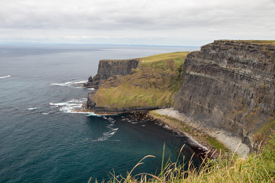 Dramatic coastal cliffs and rocky bay cove meeting the Atlantic Ocean at the Cliffs of Moher, County Clare, Ireland.