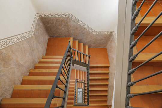 A view of a staircase with wooden steps and a metal railing. The walls are painted in a light color with decorative patterns near the top.