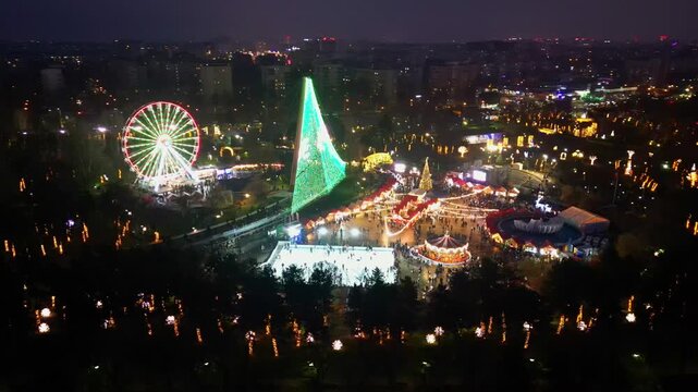 Spectacular drone shot of a crowded winter festival and Christmas market in Bucharest, Romania, illuminated by festive holiday lights and decorations at dusk.