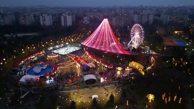 Spectacular drone shot of a crowded winter festival and Christmas market in Bucharest, Romania, illuminated by festive holiday lights and decorations at dusk.