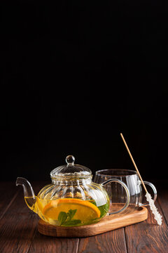 Glass teapot with refreshing citrus mint beverage and sugar stick on wooden table