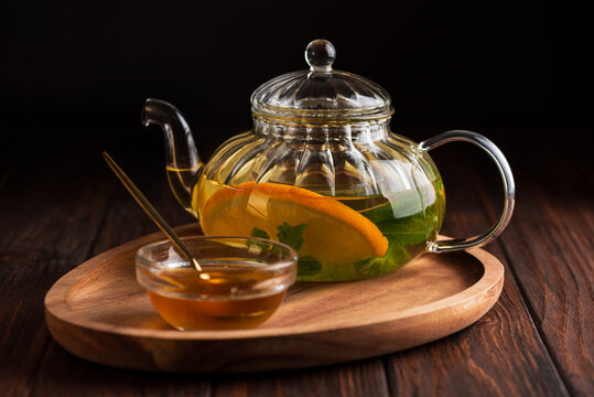Glass teapot with refreshing orange and mint infused herbal tea served with honey on wooden tray